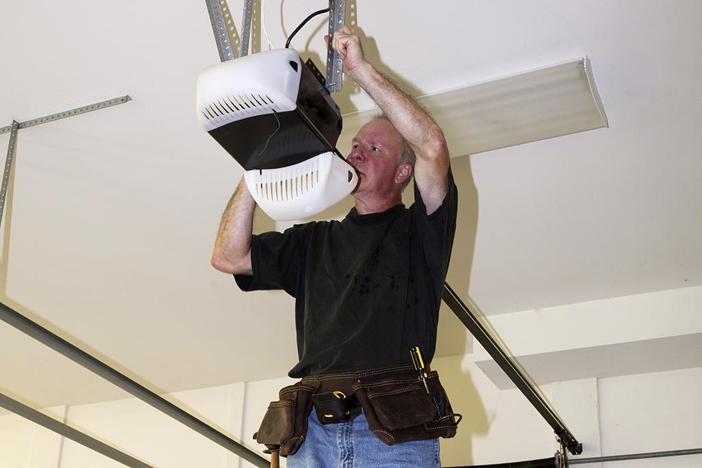 Man standing on a ladder fixing a mechanical garage door opener
